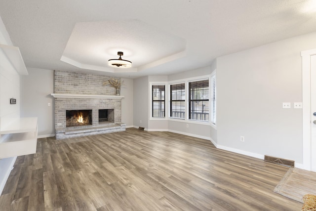 unfurnished living room featuring a raised ceiling, hardwood / wood-style floors, a brick fireplace, and a textured ceiling