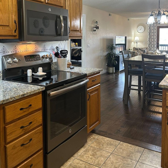 kitchen featuring light tile patterned flooring, a chandelier, decorative backsplash, stainless steel appliances, and light stone countertops