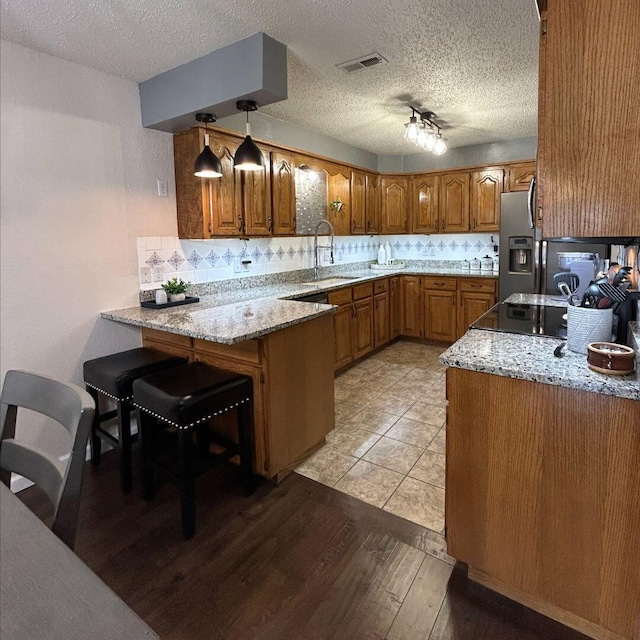 kitchen with a breakfast bar, kitchen peninsula, sink, hanging light fixtures, and stainless steel fridge with ice dispenser