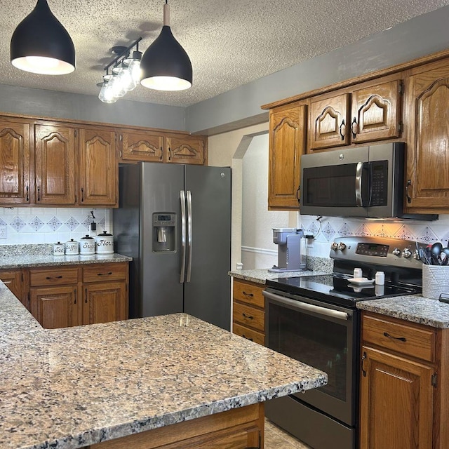 kitchen featuring stainless steel appliances, light stone counters, decorative backsplash, a textured ceiling, and decorative light fixtures