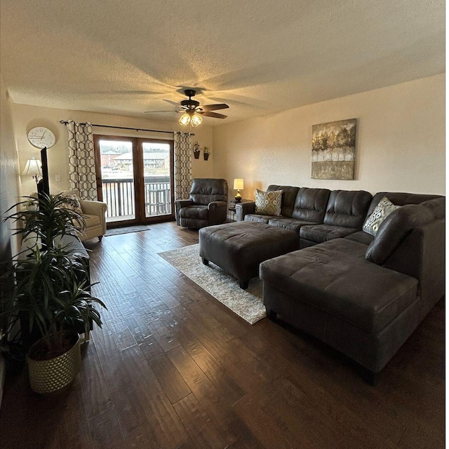 living room featuring dark wood-type flooring, ceiling fan, and a textured ceiling