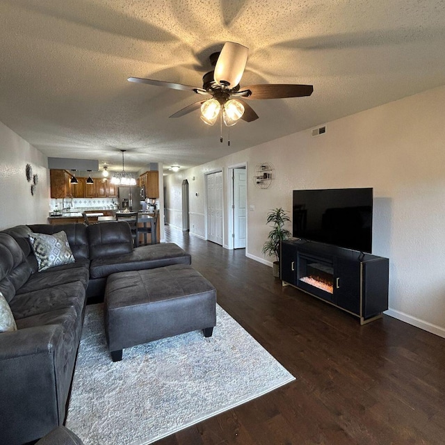 living room featuring ceiling fan, a textured ceiling, and dark hardwood / wood-style flooring