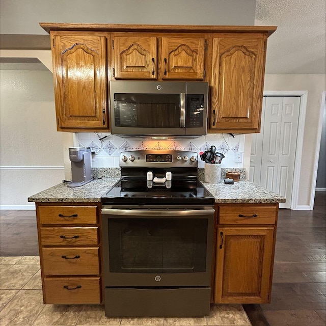 kitchen featuring stainless steel appliances, light stone counters, a textured ceiling, and decorative backsplash