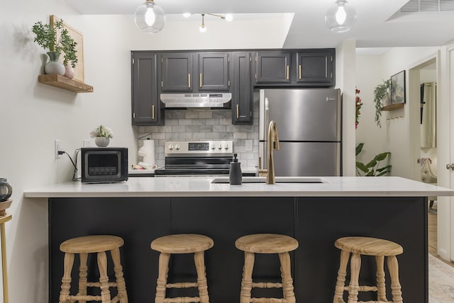 kitchen with sink, tasteful backsplash, appliances with stainless steel finishes, a kitchen breakfast bar, and kitchen peninsula