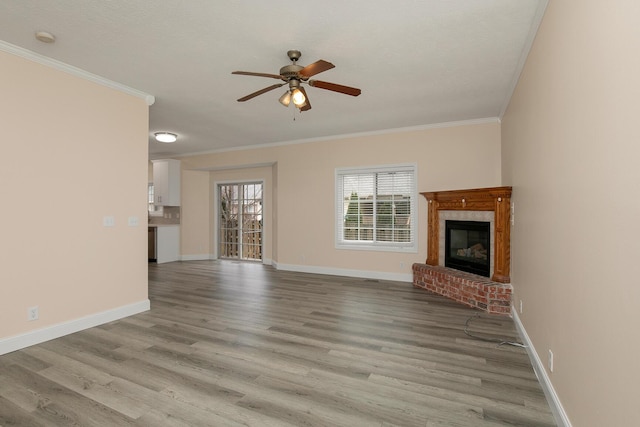 unfurnished living room with ceiling fan, ornamental molding, a brick fireplace, and light wood-type flooring