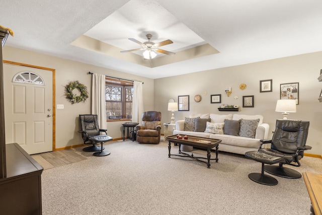 living room with a tray ceiling, ceiling fan, and carpet