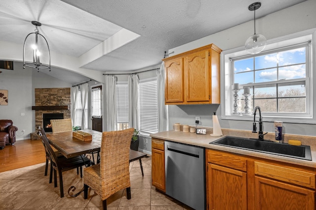 kitchen with a fireplace, sink, hanging light fixtures, stainless steel dishwasher, and a textured ceiling