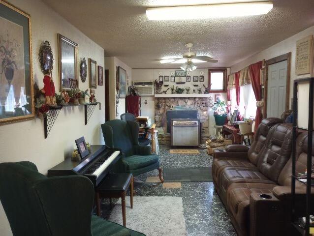 living room featuring ceiling fan, a fireplace, and a textured ceiling