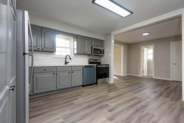 kitchen featuring a wealth of natural light, gray cabinets, decorative backsplash, and appliances with stainless steel finishes
