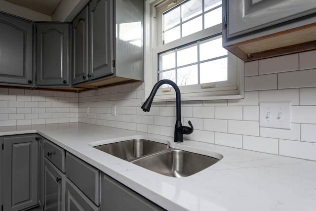 kitchen with tasteful backsplash, a sink, light stone counters, and gray cabinets
