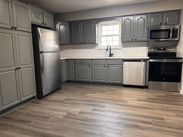 kitchen featuring gray cabinets, appliances with stainless steel finishes, a sink, light countertops, and decorative backsplash