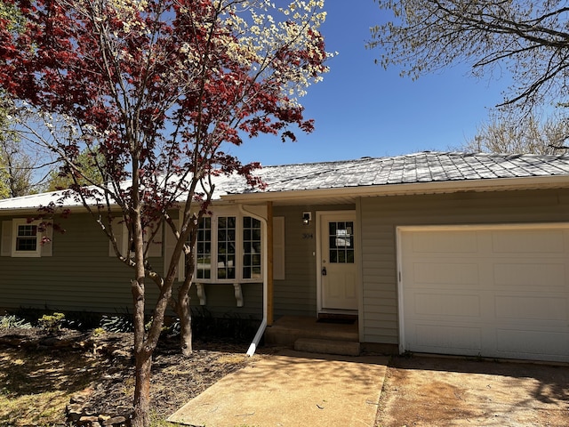 ranch-style house featuring concrete driveway, metal roof, and an attached garage