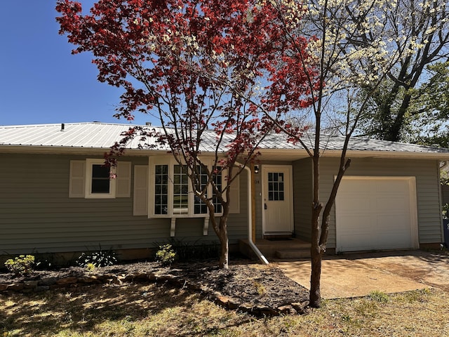 single story home with entry steps, metal roof, a garage, and concrete driveway