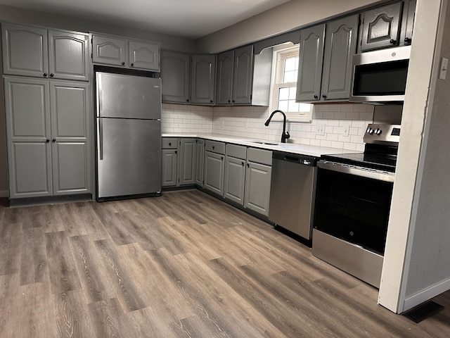 kitchen featuring tasteful backsplash, gray cabinets, appliances with stainless steel finishes, light wood finished floors, and a sink