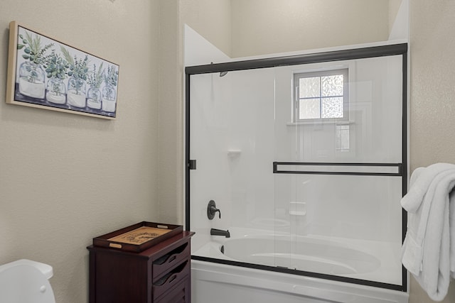 bathroom with enclosed tub / shower combo, a textured wall, and toilet