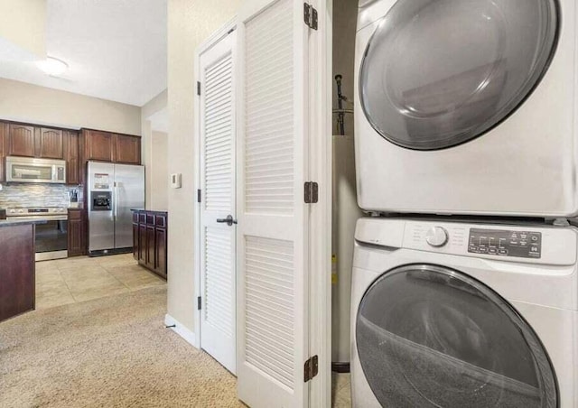 laundry room with stacked washer / dryer, laundry area, baseboards, and light tile patterned floors