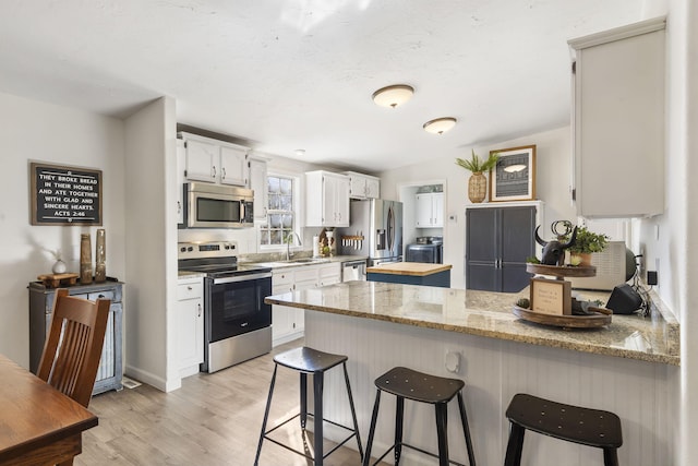 kitchen featuring sink, white cabinets, kitchen peninsula, stainless steel appliances, and light stone countertops