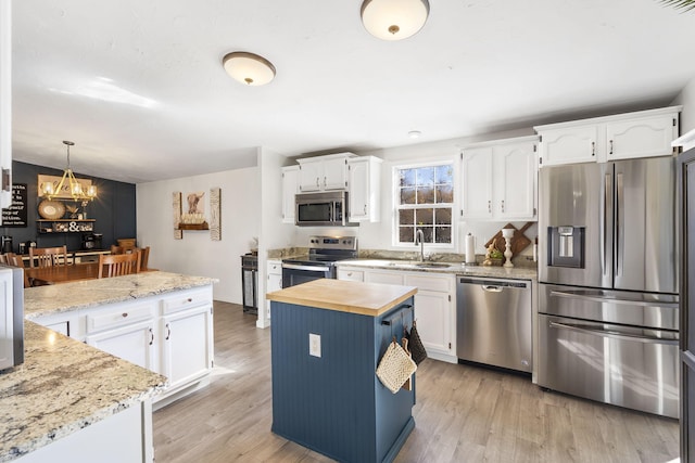 kitchen with sink, appliances with stainless steel finishes, white cabinetry, a kitchen island, and decorative light fixtures