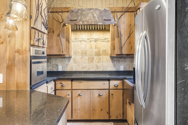 kitchen featuring stainless steel appliances, dark stone countertops, exhaust hood, and decorative backsplash