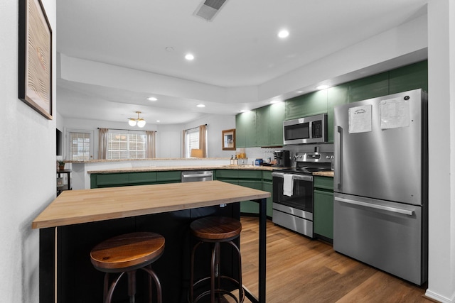 kitchen with a kitchen bar, appliances with stainless steel finishes, kitchen peninsula, green cabinets, and hardwood / wood-style flooring