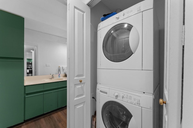 clothes washing area with stacked washer and clothes dryer, sink, and dark hardwood / wood-style flooring