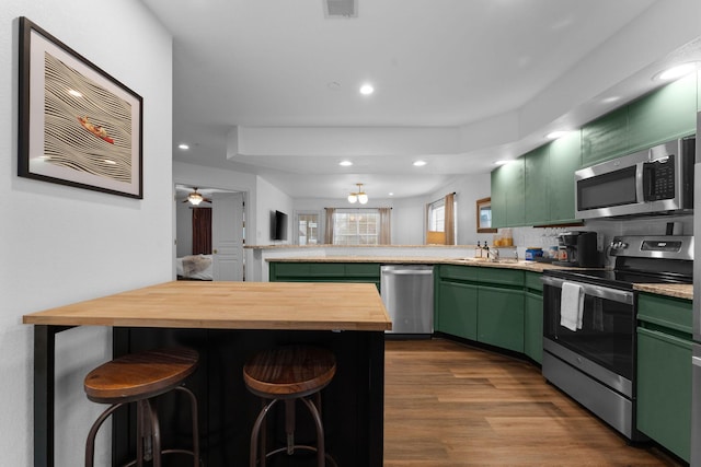 kitchen with stainless steel appliances, a breakfast bar area, butcher block counters, and green cabinets