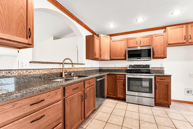 kitchen with stainless steel appliances, sink, light tile patterned floors, and dark stone counters