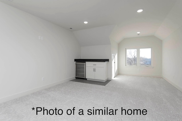 additional living space with wine cooler, vaulted ceiling, light colored carpet, and indoor bar