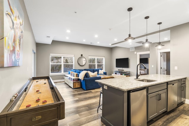 kitchen with sink, dishwasher, dark hardwood / wood-style floors, light stone countertops, and a kitchen bar