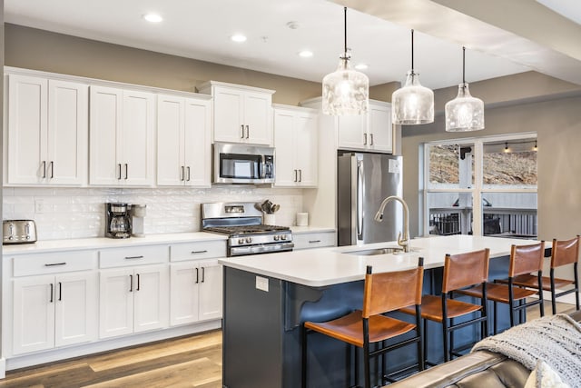 kitchen featuring white cabinetry, hanging light fixtures, a kitchen island with sink, and appliances with stainless steel finishes