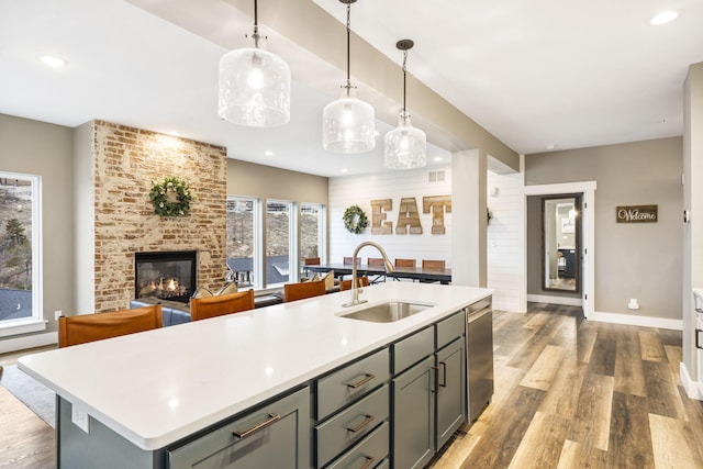 kitchen featuring an island with sink, a fireplace, sink, and hanging light fixtures