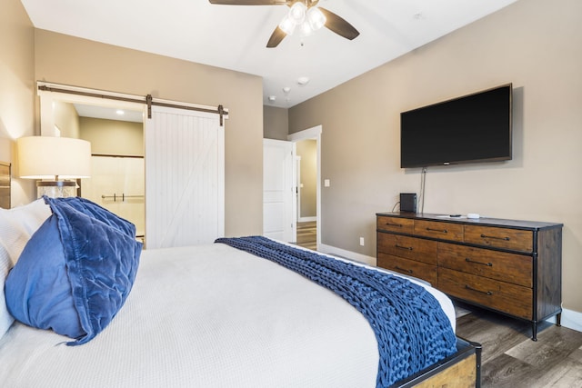 bedroom with ceiling fan, a barn door, and dark hardwood / wood-style flooring