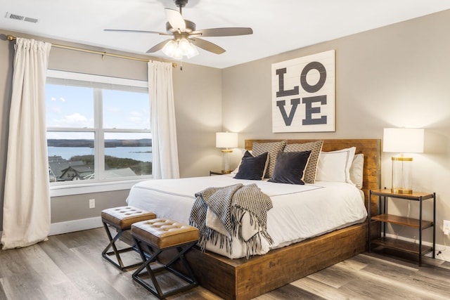 bedroom featuring a water view, ceiling fan, and hardwood / wood-style flooring