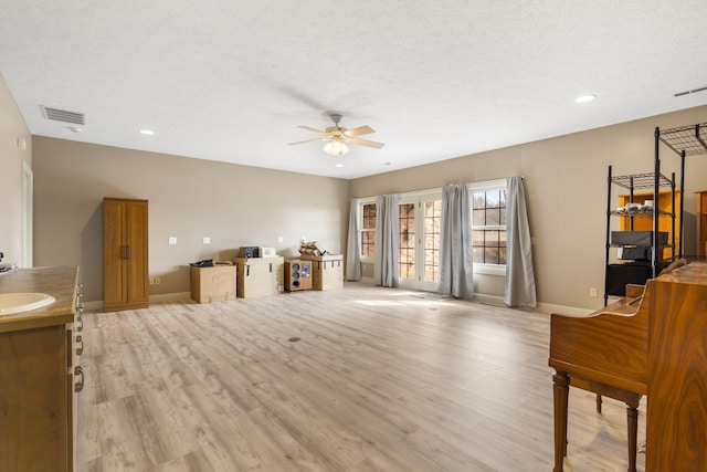 living room featuring sink, a textured ceiling, ceiling fan, and light wood-type flooring