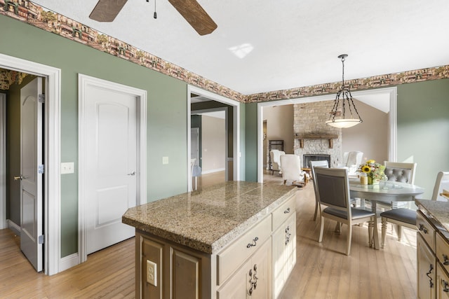 kitchen featuring decorative light fixtures, a stone fireplace, light hardwood / wood-style floors, and a center island