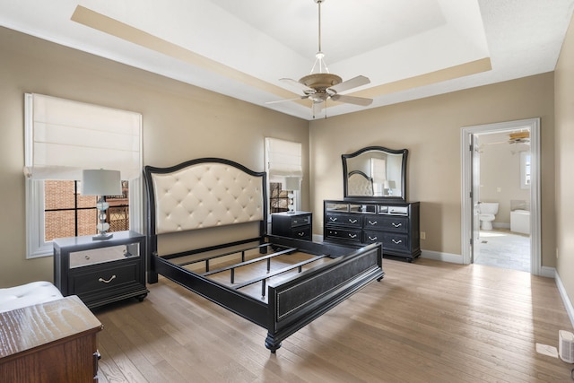 bedroom with ensuite bathroom, a tray ceiling, and hardwood / wood-style floors