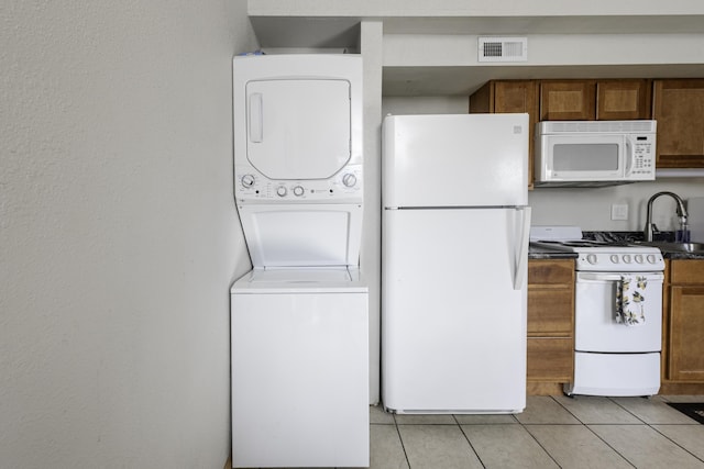 kitchen with stacked washer / drying machine, white appliances, sink, and light tile patterned flooring