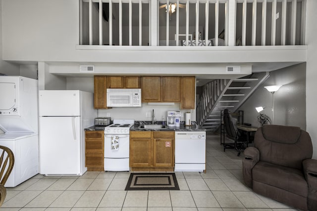 kitchen with sink, white appliances, light tile patterned floors, and stacked washing maching and dryer