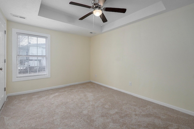 carpeted empty room with ceiling fan and a tray ceiling