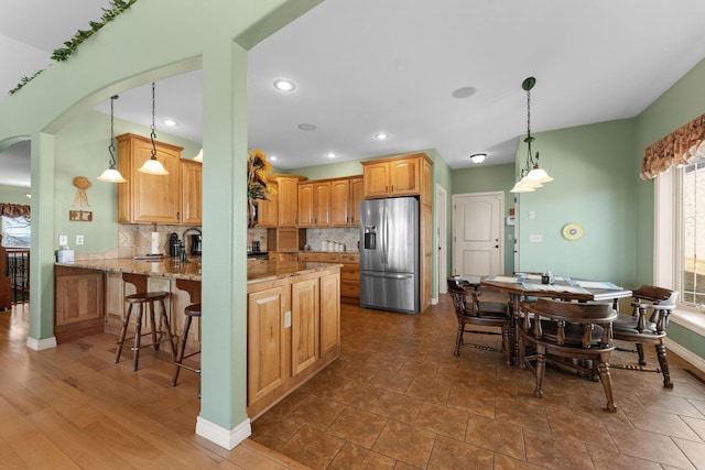 kitchen with decorative backsplash, stainless steel fridge, kitchen peninsula, and light stone countertops