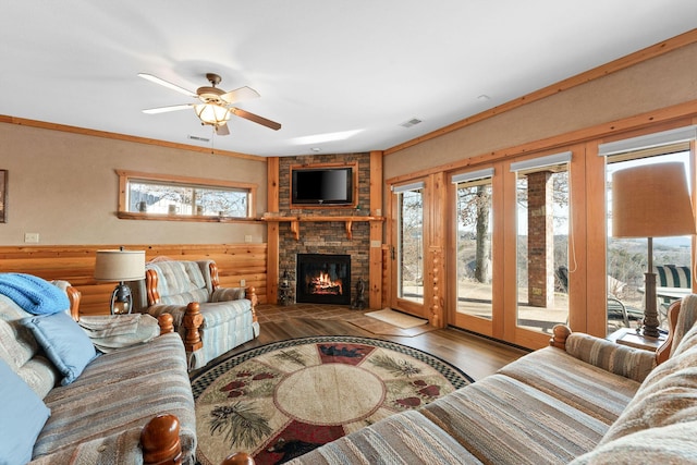 living room with hardwood / wood-style flooring, ornamental molding, a stone fireplace, and ceiling fan