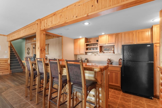 kitchen featuring black fridge, light brown cabinetry, and dark tile patterned flooring