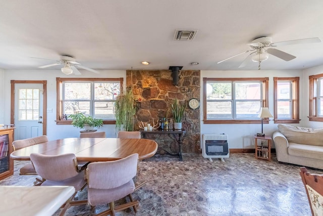 dining space with ceiling fan, a wealth of natural light, heating unit, and a wood stove