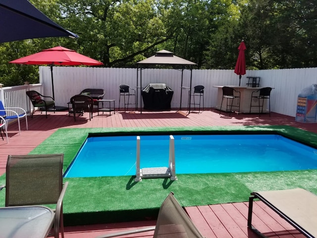 view of swimming pool featuring a wooden deck, grilling area, and an outdoor bar