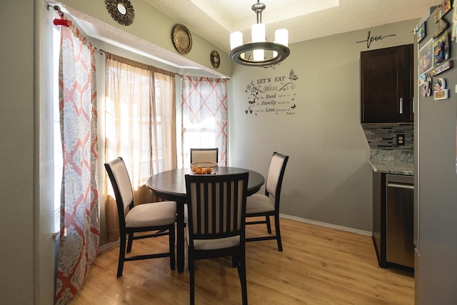 dining area featuring a healthy amount of sunlight, a tray ceiling, a chandelier, and light hardwood / wood-style floors