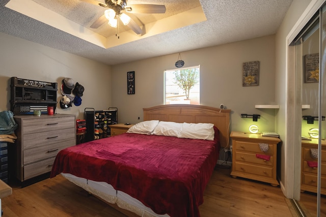 bedroom featuring a closet, hardwood / wood-style floors, a textured ceiling, and a tray ceiling