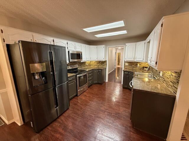 kitchen with appliances with stainless steel finishes, stone countertops, sink, white cabinets, and dark wood-type flooring