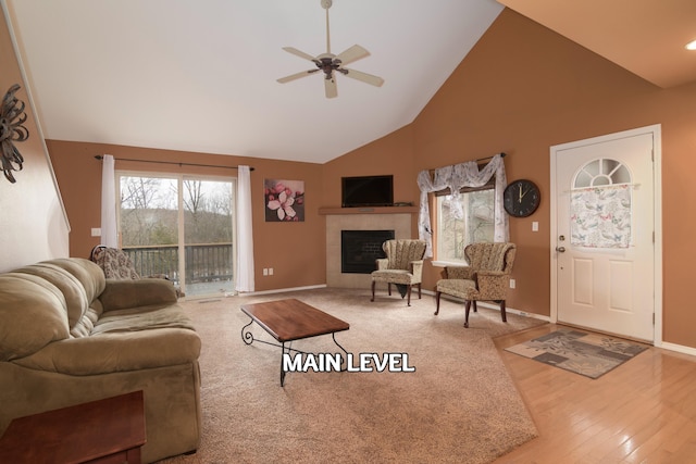 living room with a tiled fireplace, ceiling fan, hardwood / wood-style flooring, and high vaulted ceiling