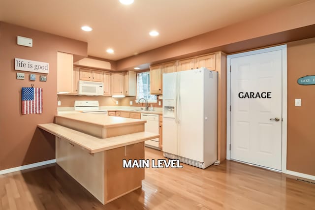 kitchen featuring white appliances, a breakfast bar, kitchen peninsula, and light brown cabinetry