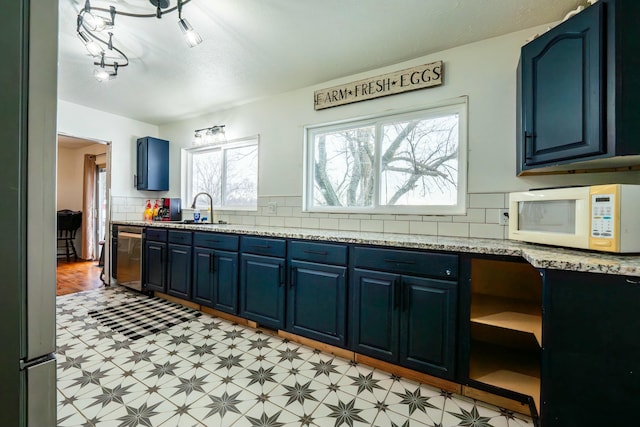 kitchen with dishwasher, sink, backsplash, light stone countertops, and blue cabinetry